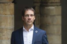 Benoiy Derenne portant une chemise blanche et une veste de costume bleu marine