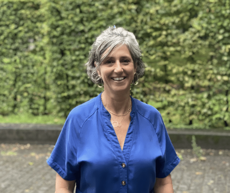 Caroline Lavadid souriant à la caméra devant une haie
