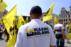 Une personne portant un t-shirt du Vlaams Belang, avec d'autres personnes autour de lui qui ajoutent le drapeau jaune du parti