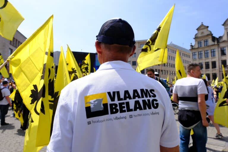 Une personne portant un t-shirt du Vlaams Belang, avec d'autres personnes autour de lui qui ajoutent le drapeau jaune du parti