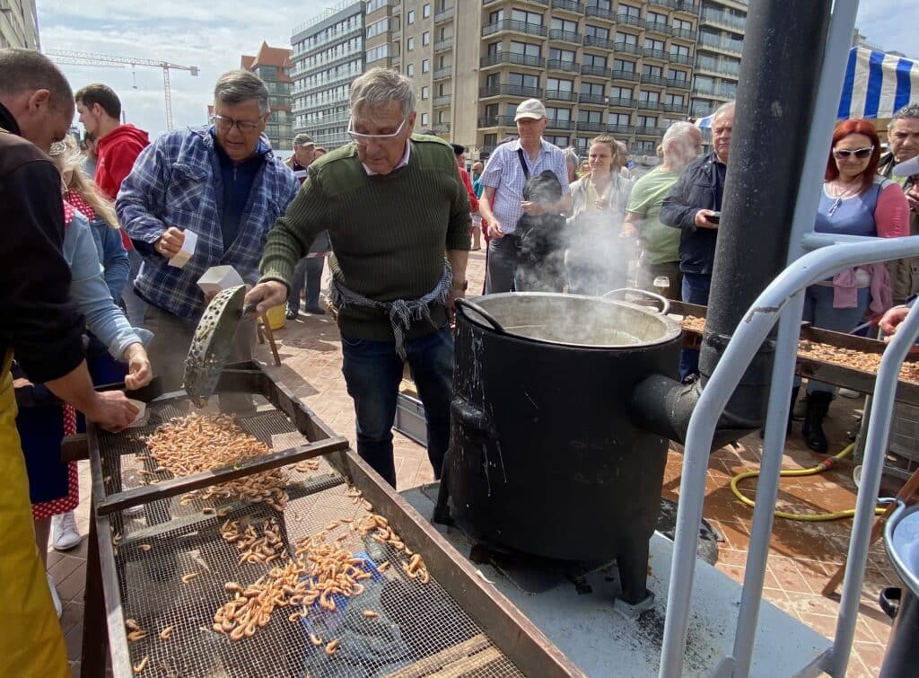 Un homme faisant cuir les crevettes dans un chaudron d'eau chaude, avec des gens autour de lui qui le regardent