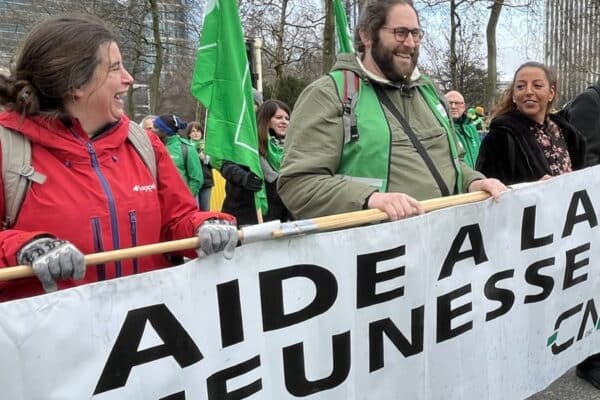 Manifestants dans la rue portant une pancarte où il est écrit Aide à la jeunesse