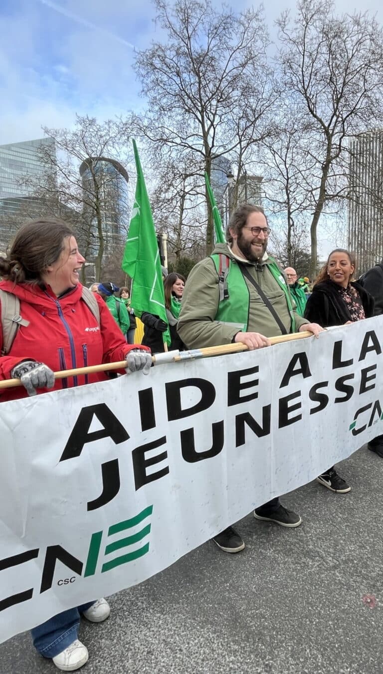 Manifestants dans la rue portant une pancarte où il est écrit Aide à la jeunesse