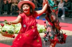 Une enfant porteuse d'un handicap accompagnée de sa maman, elles défilent sur un podium rouge avec des tenues avec des fleurs rouges et un panier de paille dans la main