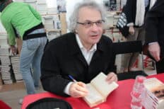 Amin Maalouf assis à une table qui dédicace un livre