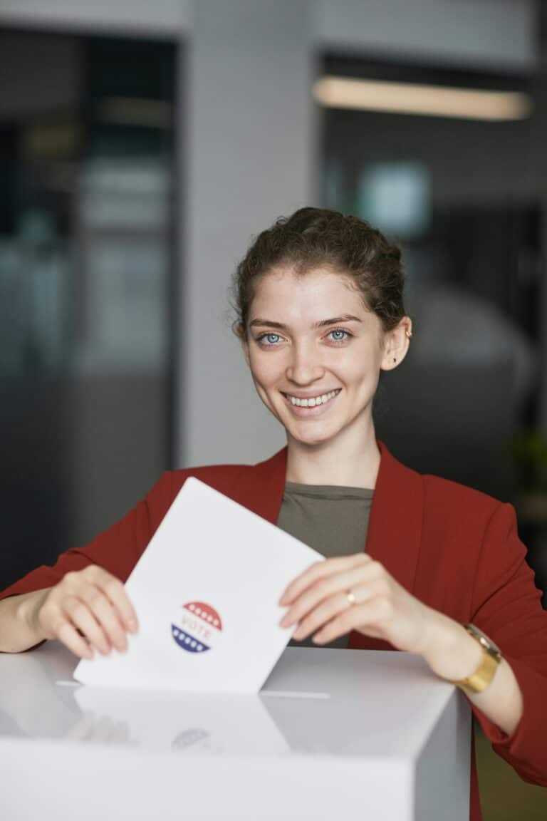 Femme souriant à la caméra et déposant un bulletin de vote dans une urne