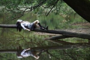 Jeune femme couchée sur un tronc d'arbre dans une forêt avec un livre sur la tête