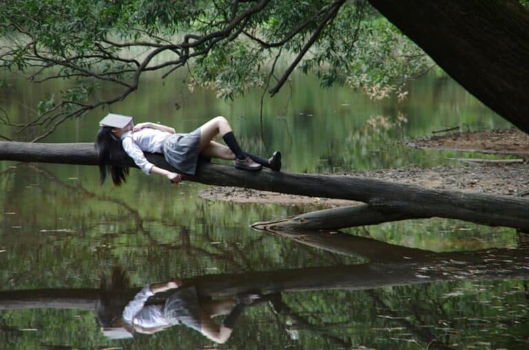 Jeune femme couchée sur un tronc d'arbre dans une forêt avec un livre sur la tête