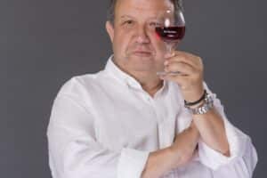 Eric Boschman portant une chemise blanche et montrant un verre de vin rouge