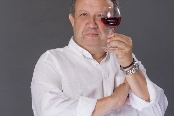 Eric Boschman portant une chemise blanche et montrant un verre de vin rouge