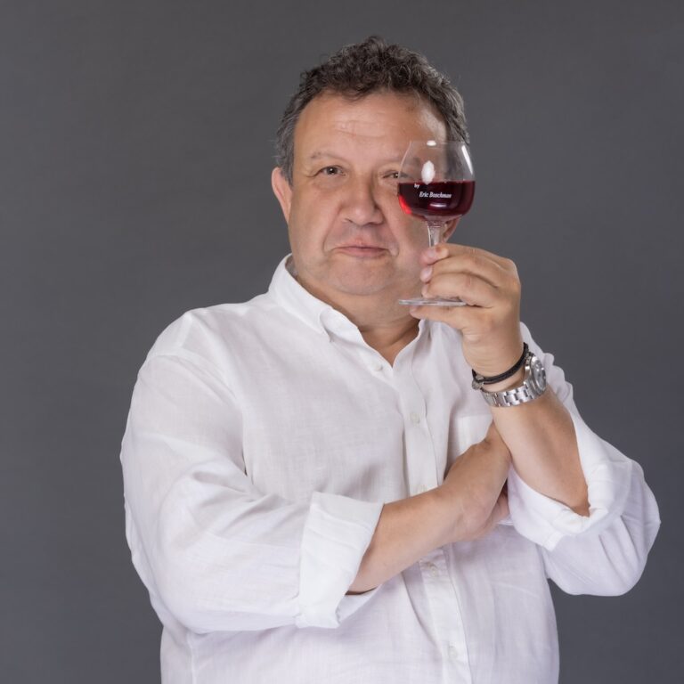 Eric Boschman portant une chemise blanche et montrant un verre de vin rouge