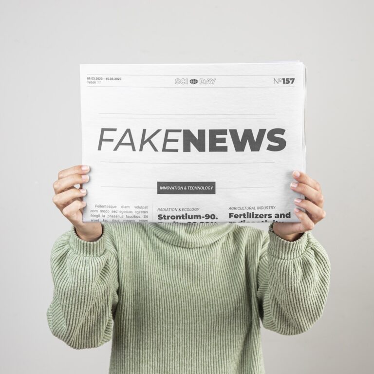 Une femme au pull vert cachant sa tête avec un journal sur lequel est écrit "Fake News"