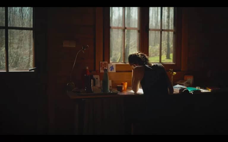Image tirée du film Wild Women, une femme de dos se trouve seule dans une pièce, assise à un bureau, la main sur la tête