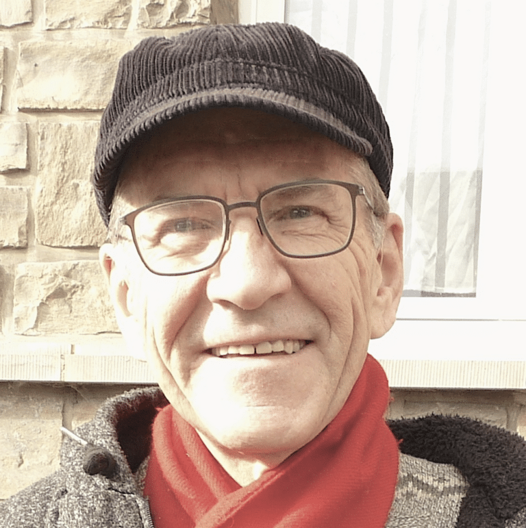 André Antoine portant un chapeau et des lunettes, souriant à la caméra