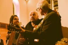 Une femme et deux hommes se tiennent l'un à côté de l'autre, l'un des deux hommes joue de la guitare.