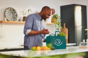 Un homme dans une cuisine regardant le contenu de son sac Too good to go