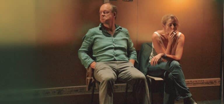 Un homme et une femme assis sur un banc. La femme fume une cigarette.