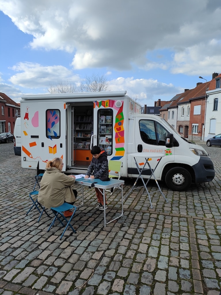 La camionnette "bibliobus" avec une femme et un enfant devant qui regarde des livres sur une petite table