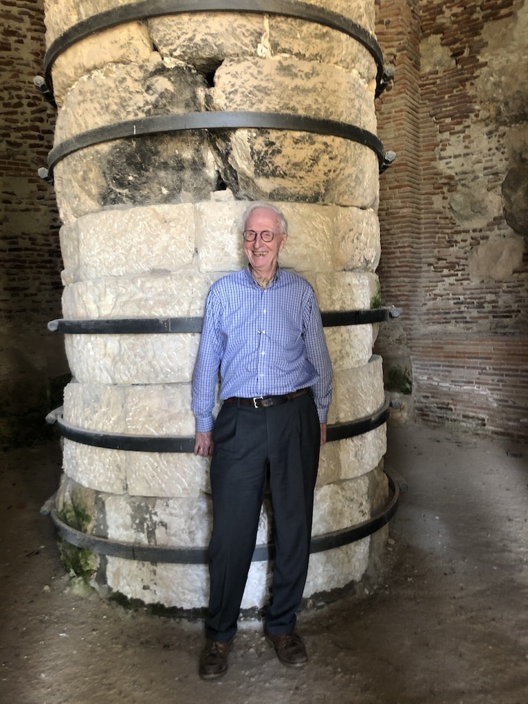 Marc Luyckx souriant et se tenant devant une grosse colonne en pierre beige clair