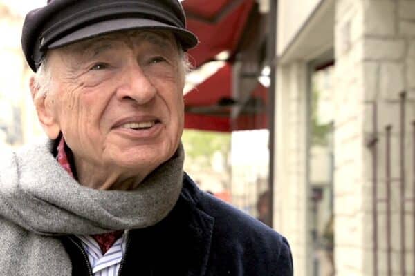 Edgar Morin portant un béret et une écharpe grise, dans une rue commerciale