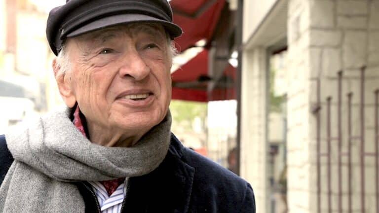 Edgar Morin portant un béret et une écharpe grise, dans une rue commerciale