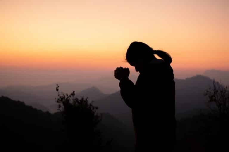 Silhouette d'une femme priant devant des montagnes et un ciel de couleurs