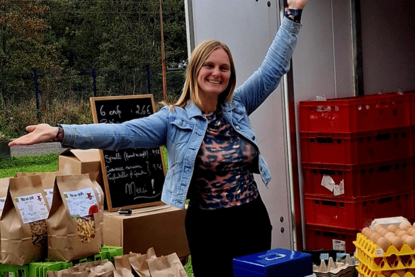 Une femme souriant, les bras vers le haut, derrière une table avec des produits bio dessus