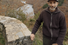 Cassingena Trévédy appuyé sur un muret, avec des arbres et un cours d'eau derrière lui