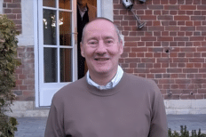 Jean Marc Mahy souriant à la caméra, devant la bâtisse d'une maison