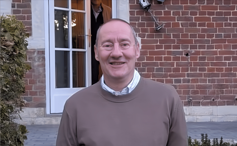 Jean Marc Mahy souriant à la caméra, devant la bâtisse d'une maison