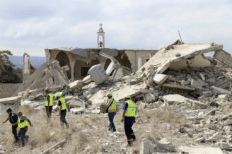 Paysage dévasté de ruines avec sept hommes portant des gilets jaunes fluo qui marchent dans les décombres