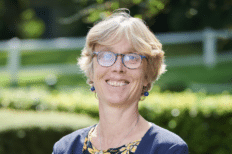 Marthe Nyssens souriant à la caméra, à l'extéirue devant des buissons et des arbres verts