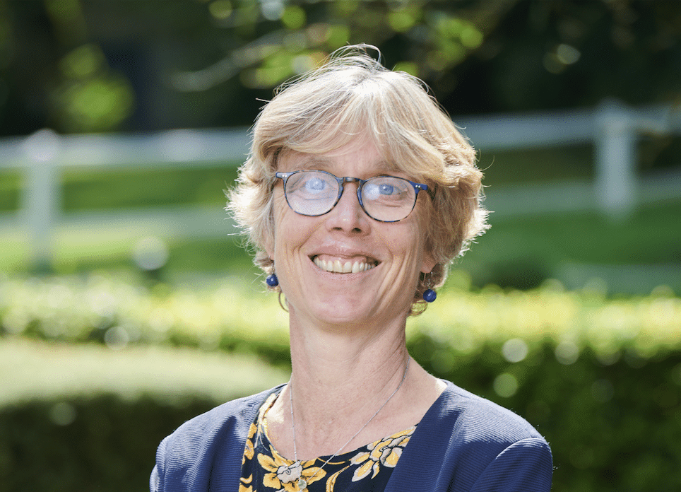 Marthe Nyssens souriant à la caméra, à l'extéirue devant des buissons et des arbres verts