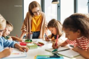 Une institutrice et 4 élèves autour d'une table en train de faire leurs devoirs