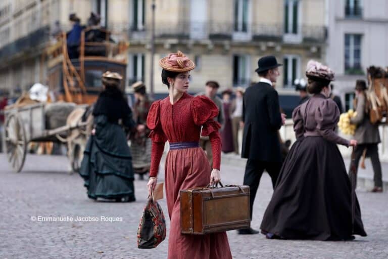 Une femme en tenue d'époque rouge au milieu d'une rue, entourée d'autres personnes en tenue d'époque également