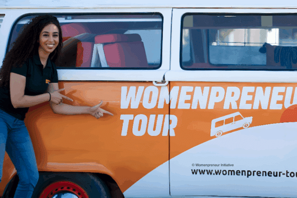 Une femme se tenant devant une camionnette orange et blanche sur laquelle il est inscrit "womenpreneur tour"