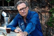 Photo de Serge Van Laeken dit "Marka" portant une chemise en jeans bleue. Il est à l'axtérieur accoudé sur une table avec une tasse posée dessus