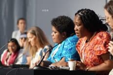 Des femmes alignées et assises les unes à côté des autres dont une a un micro devant elle et parle