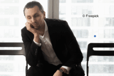 Image d'un homme assis en costume sur une chaise, la main sous la tête