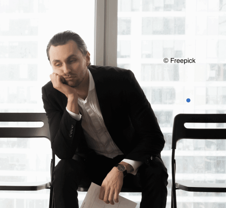 Image d'un homme assis en costume sur une chaise, la main sous la tête