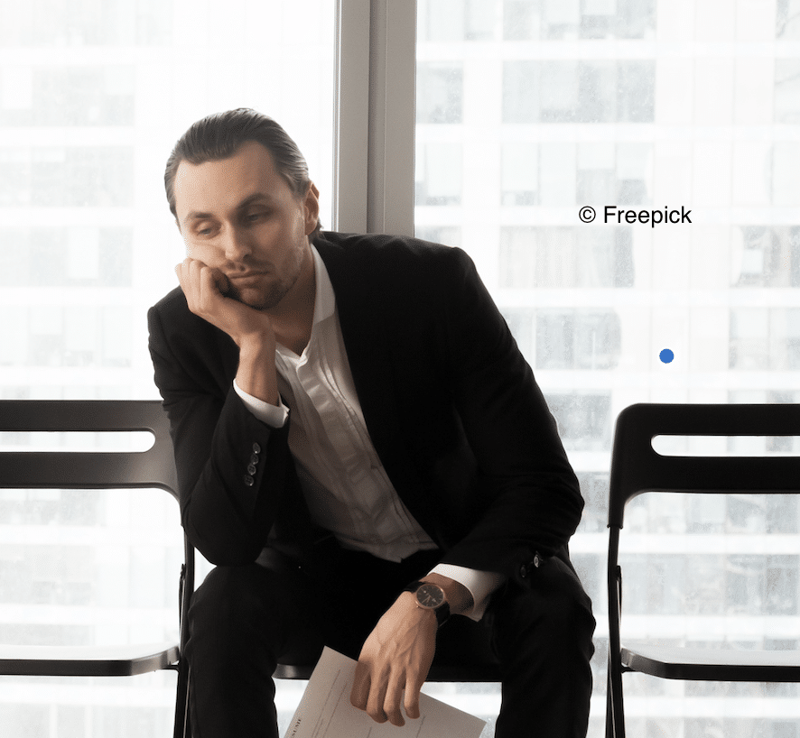 Image d'un homme assis en costume sur une chaise, la main sous la tête