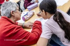 Une femme à côté d'une jeune enfant qui écrit sur un banc d'école
