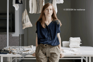 Vanessa Collignon appuyée sur une table et des vêtements accrochés sur un portique