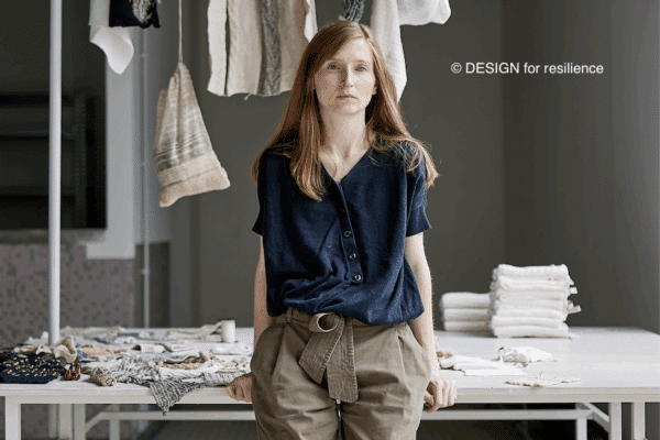 Vanessa Collignon appuyée sur une table et des vêtements accrochés sur un portique