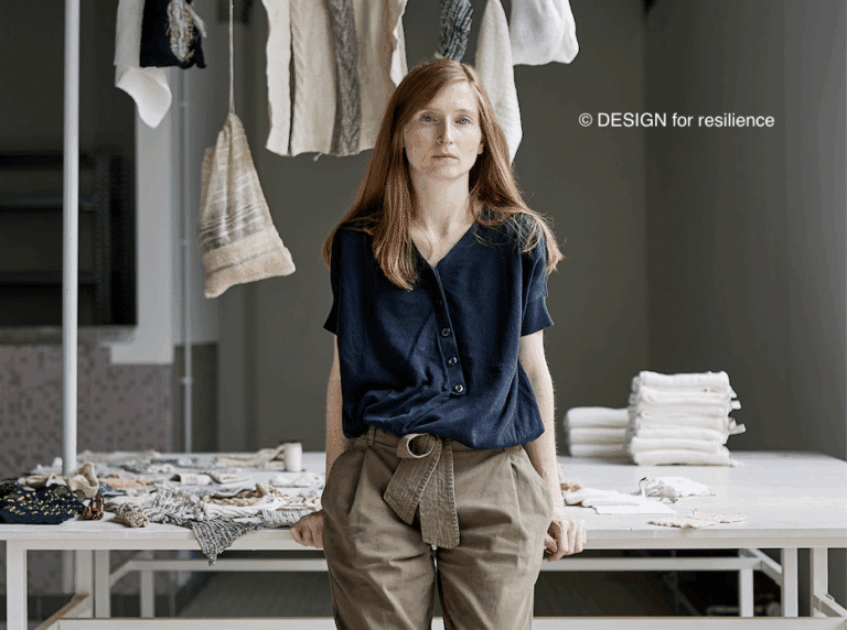 Vanessa Collignon appuyée sur une table et des vêtements accrochés sur un portique