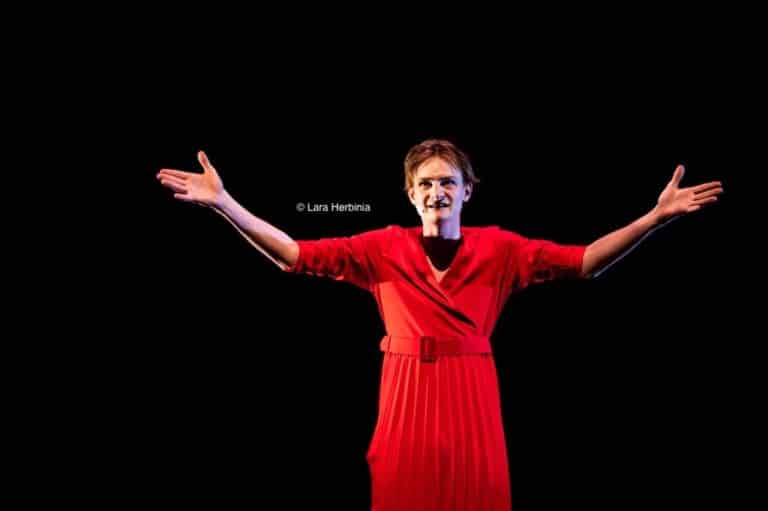 Une comédienne les bras écartés devant un fond noir