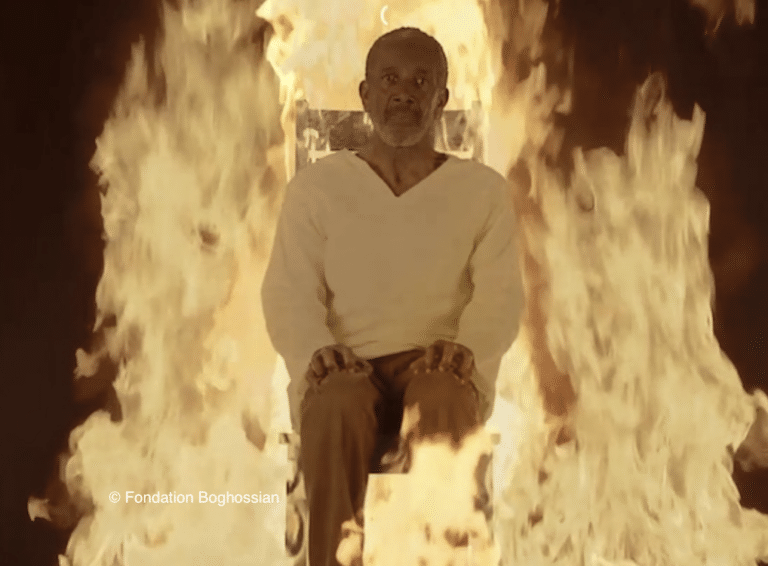 Un homme assis sur une chaise avec des flammes derrière lui