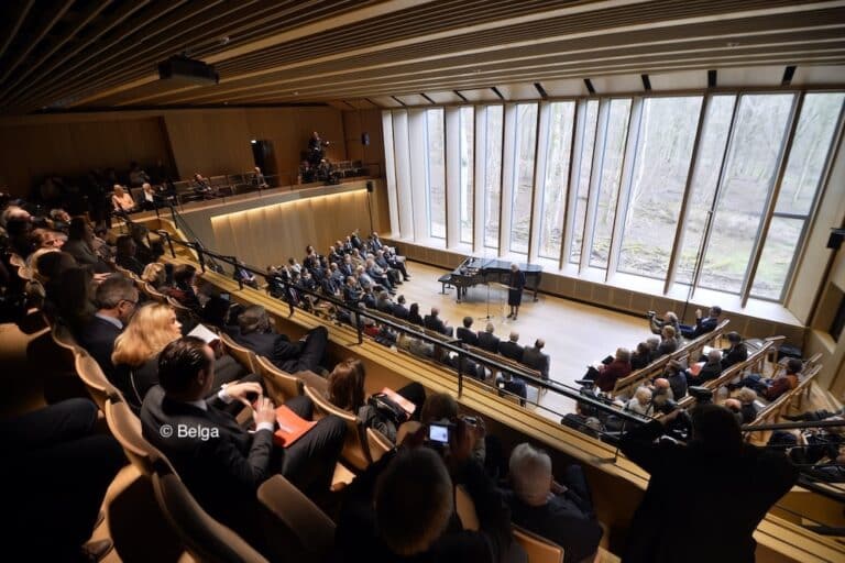 Une personne debout devant un pupitre et d'autres personnes autour assises qui l'écoutent