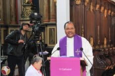 Un prêtre et une caméra derrière lui qui filme la messe
