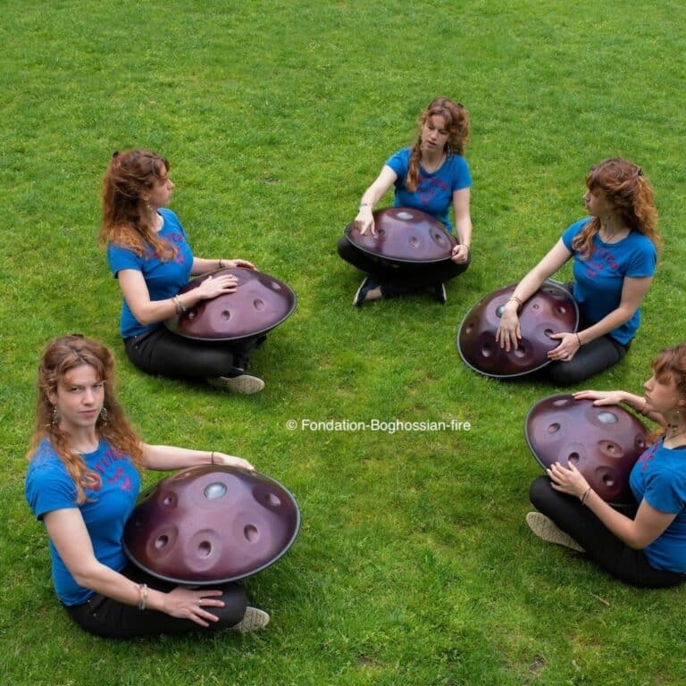 Plusieurs femmes assises dans l'herbe en train de jouer du handpan
